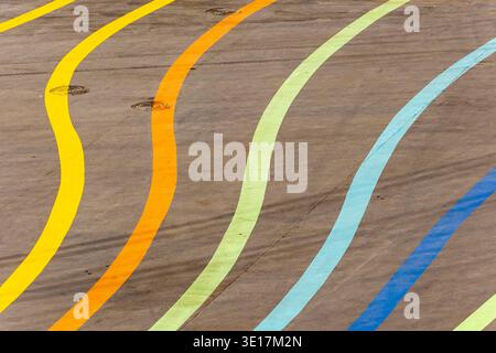 An empty asphalt surface is decorated with colorful, curved lines in yellow, orange, green, blue, and brown, creating a vibrant and dynamic pattern th Stock Photo