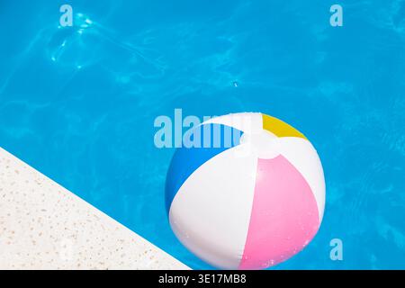 A vibrant, inflatable beach ball floats in a clear blue swimming pool on a sunny summer day, creating a refreshing scene perfect for leisure and relax Stock Photo