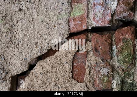 Close-up of a deep crack in an old brick wall covered with thick plaster. Concept of structural damage, building decay, and renovation needs Stock Photo