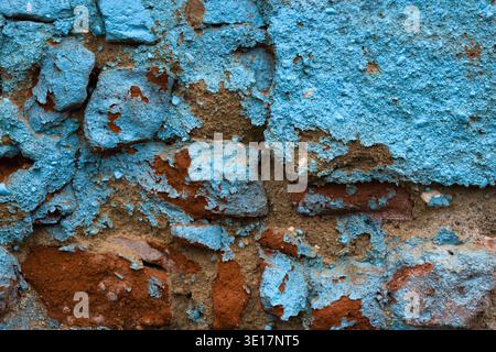 Macro texture of a crumbling brick wall with peeling blue paint and graffiti. Close up of damaged masonry and weathered exterior surface Stock Photo