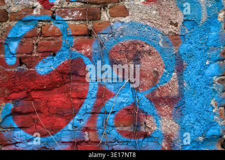 Macro texture of a red brick wall with colorful blue and red graffiti. Close up of weathered masonry and urban street art on a crumbling surface Stock Photo