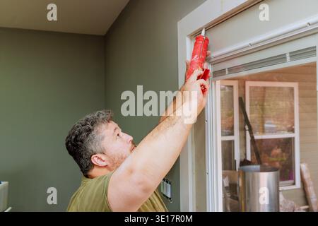 Contractor is using caulk gun to seal gaps in window frame at his house Stock Photo
