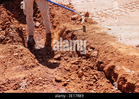 Worker uses shovel to dig trench in ground at construction site Stock Photo