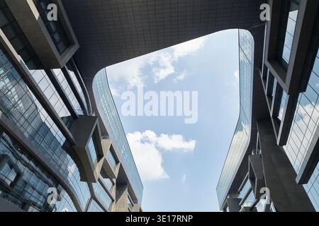 Upward view between curving modern facades and blue sky. Stock Photo