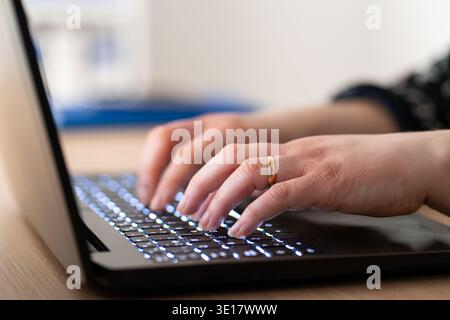 Close-up of a businesswoman working late typing on a blue backlight, backlit on laptop keypad. Stock Photo