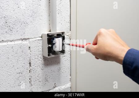 Electrician mounting electric sockets on the white wall. Electrician wiring a new build. Worker installing socket in new house. Man installing light s Stock Photo