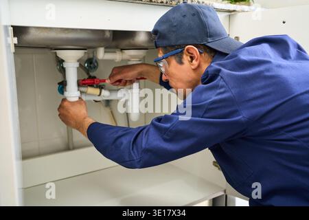 Plumbing, pipes and maintenance with man in kitchen for repair, industrial and inspection. Handyman, tools and safety with male plumber fixing sink fo Stock Photo