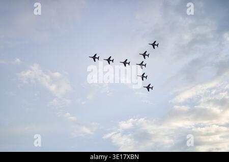 Eight military jet aircraft flying in tight V-formation against a partly cloudy sky. The aerobatic team performs a precision maneuver with the... Stock Photo