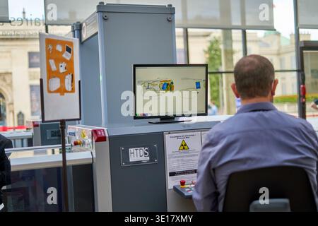 – MARCH 19, 2026: Security officer monitoring X-ray scanner machine at checkpoint. Rear view of male operator in blue shirt... Stock Photo