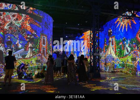 Visitors explore a vibrant immersive digital art exhibition featuring large-scale projections of colorful mosaic-style artwork covering curved... Stock Photo