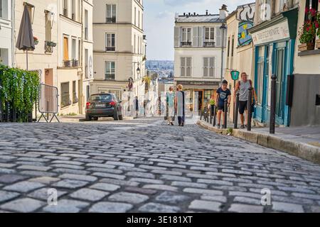 A picturesque cobblestone street in Montmartre, Paris, France, winds uphill between traditional cream-colored Parisian apartment buildings with... Stock Photo