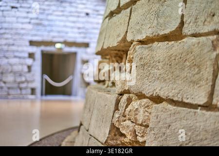 Ancient stone structure with weathered limestone blocks displayed in museum interior, showcasing archaeological artifact with detailed masonry... Stock Photo