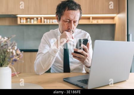 Focused businessman using smartphone with laptop on desk, symbolizing technology, online communication, productivity, and contemporary professional wo Stock Photo