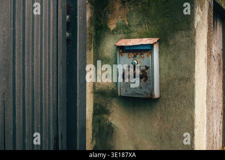Vintage, heavily rusted metal mailbox mounted on a rough concrete wall painted green-gray. Selective focus. Stock Photo
