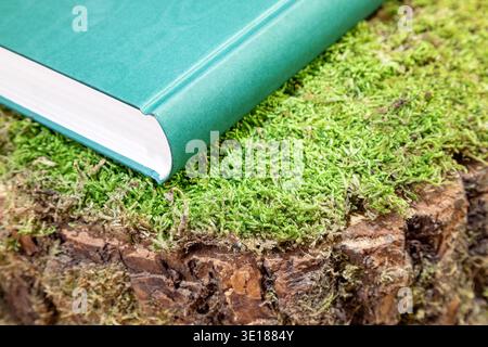 hardcover book with green cover on a mossy tree stump Stock Photo