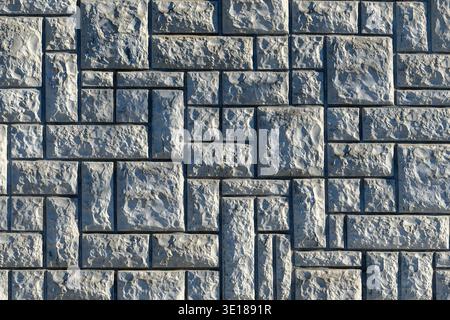 Architectural detail of decorative stone cladding in interlocking rectangular layout, weathered texture highlighted by natural sunlight, as background Stock Photo