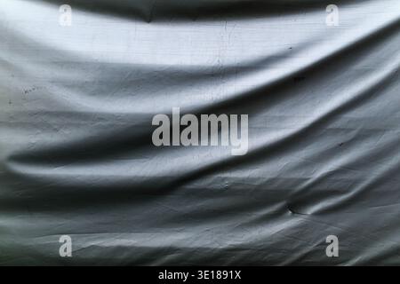 Close-up of wrinkled gray tarpaulin plastic sheet, showing folds, creases, and rough texture used as an abstract industrial background. Selective focu Stock Photo