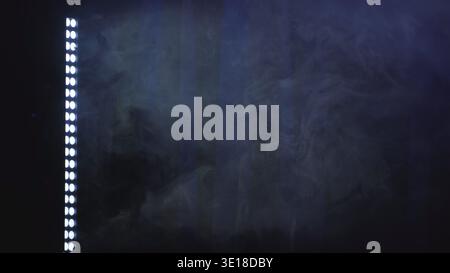 Modern LED light bar illuminating swirling blue smoke on a dark, atmospheric background Stock Photo