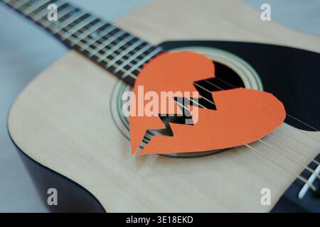 Broken red paper heart on acoustic guitar strings. Heartbreak playlist. Concept of heartbreak, emotional pain, breakup. Stock Photo