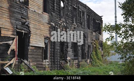Charred remains of an old log cabin building after a fire, showing decay and ruin Stock Photo