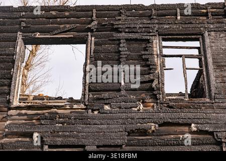 Burnt house wall with charred wooden logs and empty windows after fire disaster Stock Photo
