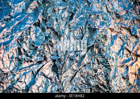 Crumpled aluminum foil surface reflecting light with abstract blue and orange metallic texture Stock Photo