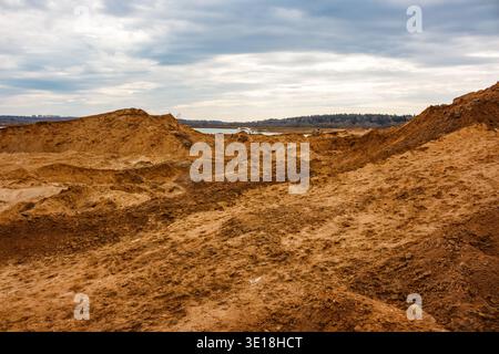 Barren industrial landscape with massive sand dunes and excavated earth. A vast quarry site under a dramatic cloudy sky, reflecting raw, disturbed ter Stock Photo