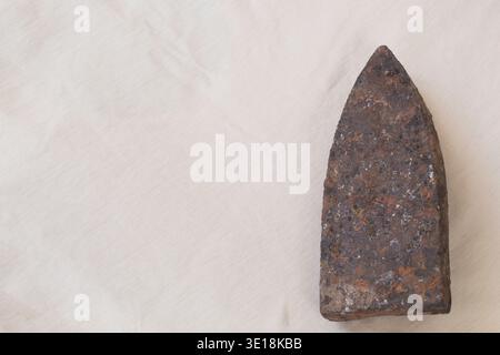 Antique rusted cast-iron flatiron soleplate with heavy patina on light linen fabric. Stock Photo