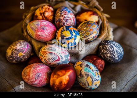 A collection of decorative silk-dyed Easter eggs nestled in a rustic woven basket on a linen cloth. Stock Photo