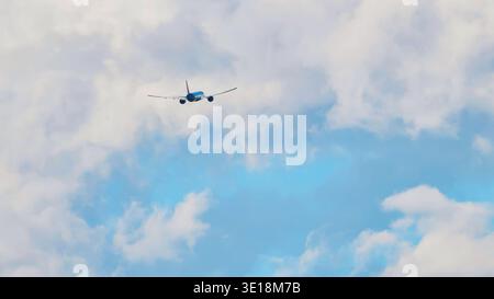 Passenger airplane flying away through white clouds in a blue sky Stock Photo