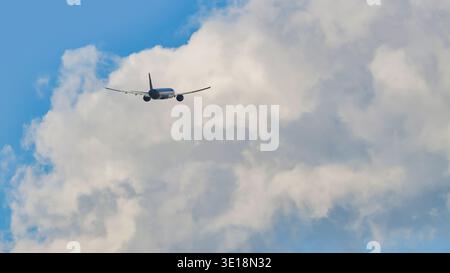 Commercial passenger airplane flying away into large white clouds in a bright blue sky Stock Photo