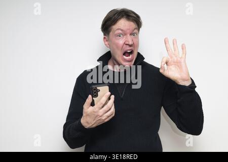 Happy Scandinavian mid adult man using phone against white background making OK sign gesture Stock Photo