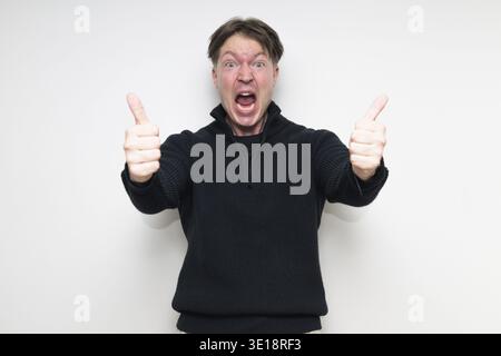 Scandinavian mid adult man smiling in black sweater portrait against white studio background giving thumbs up gesture Stock Photo