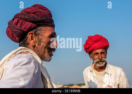 Two men wearing brightly coloured turbans look in different directions against a clear blue sky during the annual Pushkar Camel Fair. Pushkar Rajastha Stock Photo