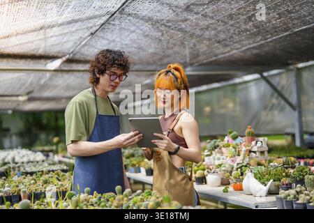 Young Asian Man and Woman Plant Research Working Together in Greenhouse Inspecting Blooming Cactus Flowers with Tablet Eco-Friendly Research and Data Stock Photo