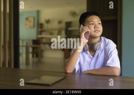 Thai Student in School Uniform Studying in Library Using Phone Stock Photo