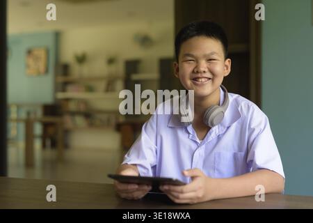 Thai Student in School Uniform Studying in Library Using Tablet Computer Stock Photo