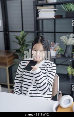 Asian Woman Engaging with Voice Assistant on Smartphone in Modern Home Stock Photo