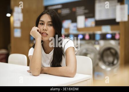 Young woman sitting in laundry shop doing housework Stock Photo