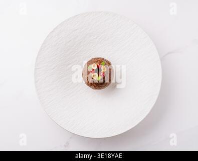 A round, chocolate dessert topped with colorful decorations sits on a sleek white plate Stock Photo