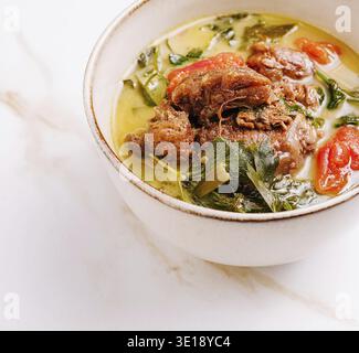 A hearty meat stew filled with tender chunks of meat, vibrant tomatoes, and fresh greens sits in a rustic bowl. The rich broth exudes warmth and comfo Stock Photo