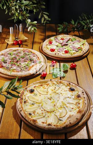 Three artisanal pizzas are displayed on wooden boards, topped with fresh ingredients. Cherry tomatoes and herbs surround the pizzas, highlighting thei Stock Photo