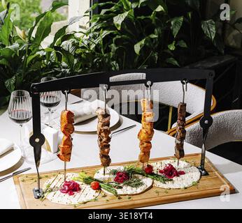 A wooden platter features an array of skewers with marinated meats, garnished with herbs, set in a stylish dining space. Natural light filters through Stock Photo