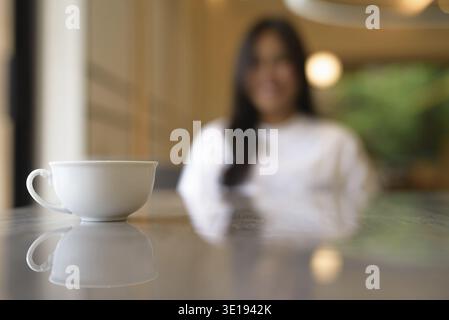 Coffee Cup in Focus with Smiling Young Thai Woman in Background Concept Stock Photo