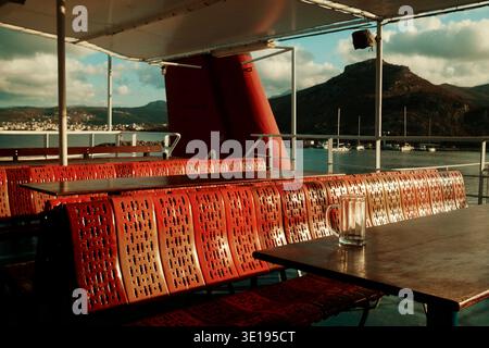 Rows of seats on ferry deck with dramatic light and shadows, Crete, Greece, with mountains in background. Stock Photo