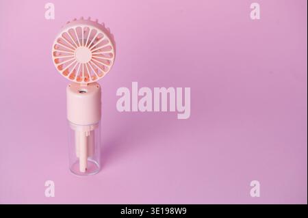 A small fan device with a mist sprayer sits on a pink surface. Stock Photo