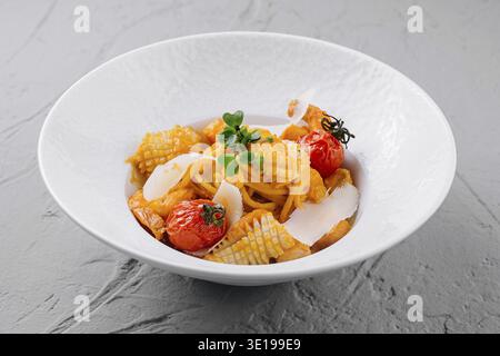 Exquisite pasta with roasted cherry tomatoes, herbs, and parmesan in a white bowl, fine dining Stock Photo