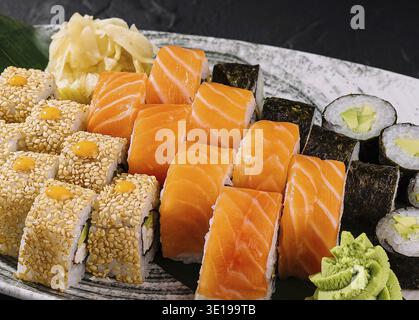 Variety of sushi rolls on a ceramic plate, elegantly presented against a black slate background Stock Photo