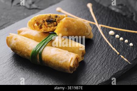 Delicious golden spring rolls with visible filling served on a dark slate board Stock Photo