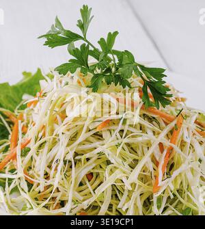 Fresh salad with shredded white cabbage, grated carrots and dill on white plate, served on wooden table Stock Photo